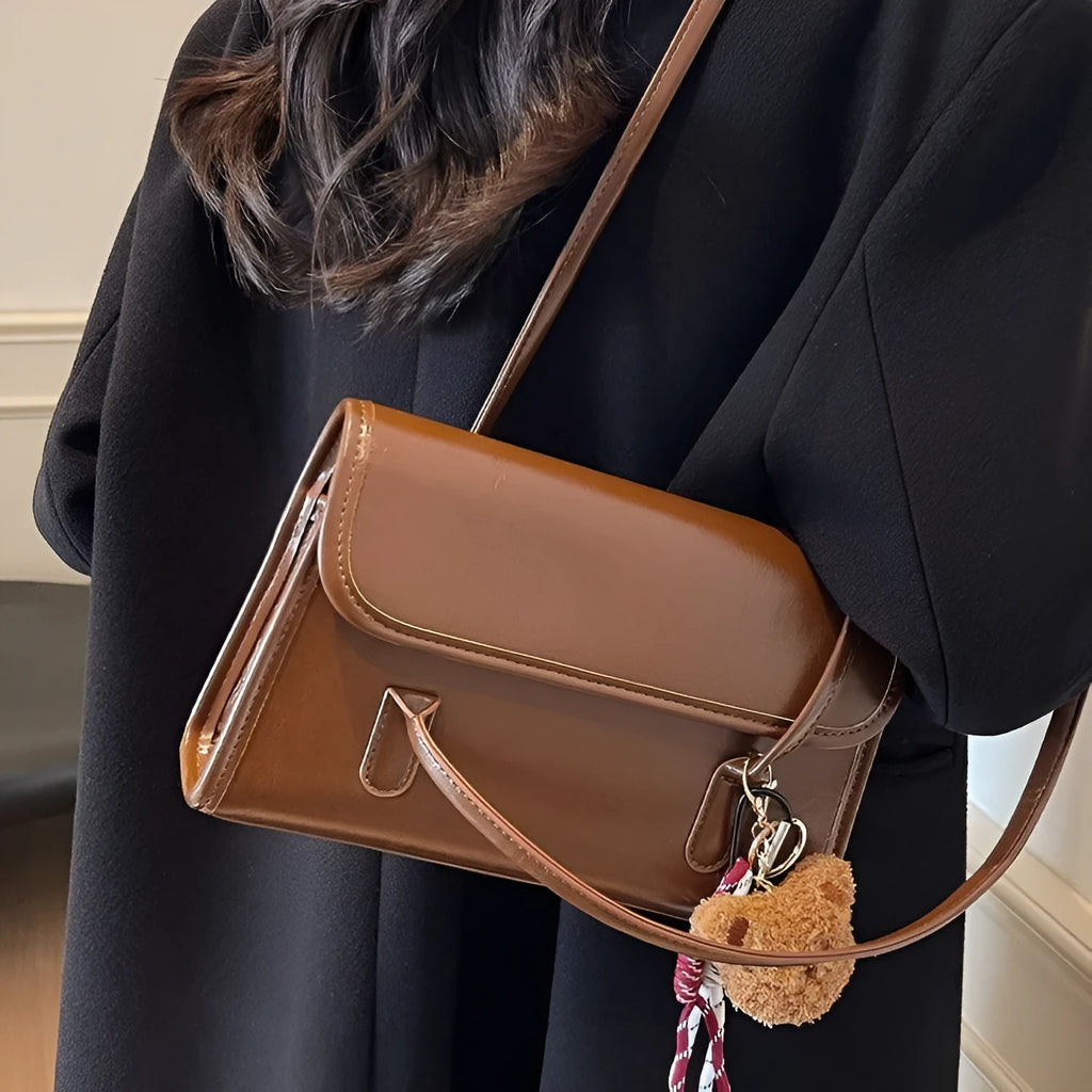 Brown women's square shoulder bag with pendant detail and adjustable crossbody straps on table