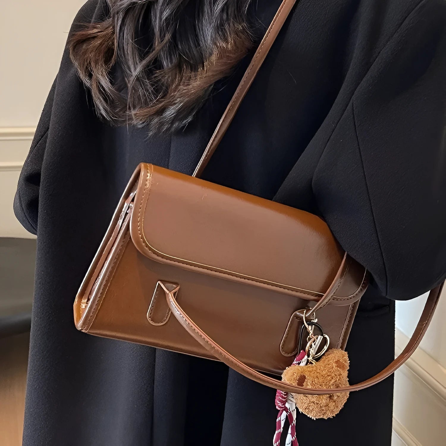 Brown women's square shoulder bag with pendant detail and adjustable crossbody straps on table