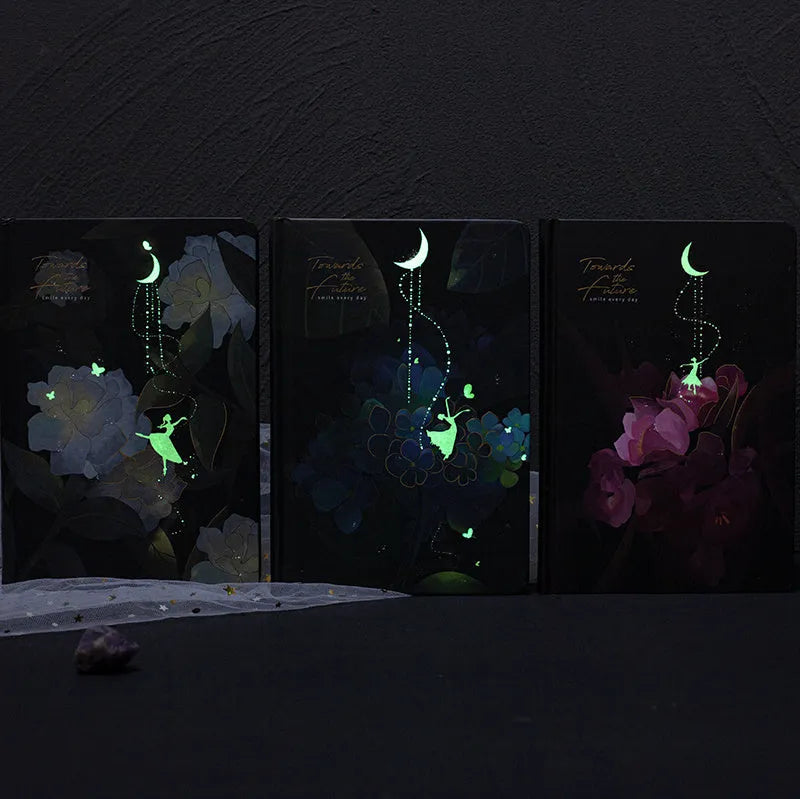 A5 notebook with luminous reflective cover shown in four colours: deep blue, gold, light blue, purple, open to reveal pages with colour illustrations.
