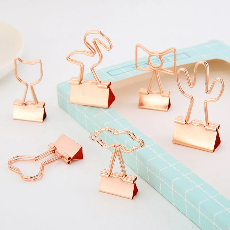 Small gold metal office clip with a long tail handle, shown in decorative bow, cactus, cat, flamingo, and love shapes.