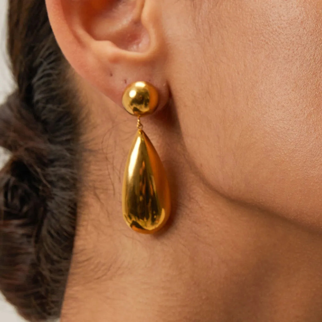 A pair of gold-coloured stainless steel earrings featuring geometric hemisphere shapes forming a water droplet design.