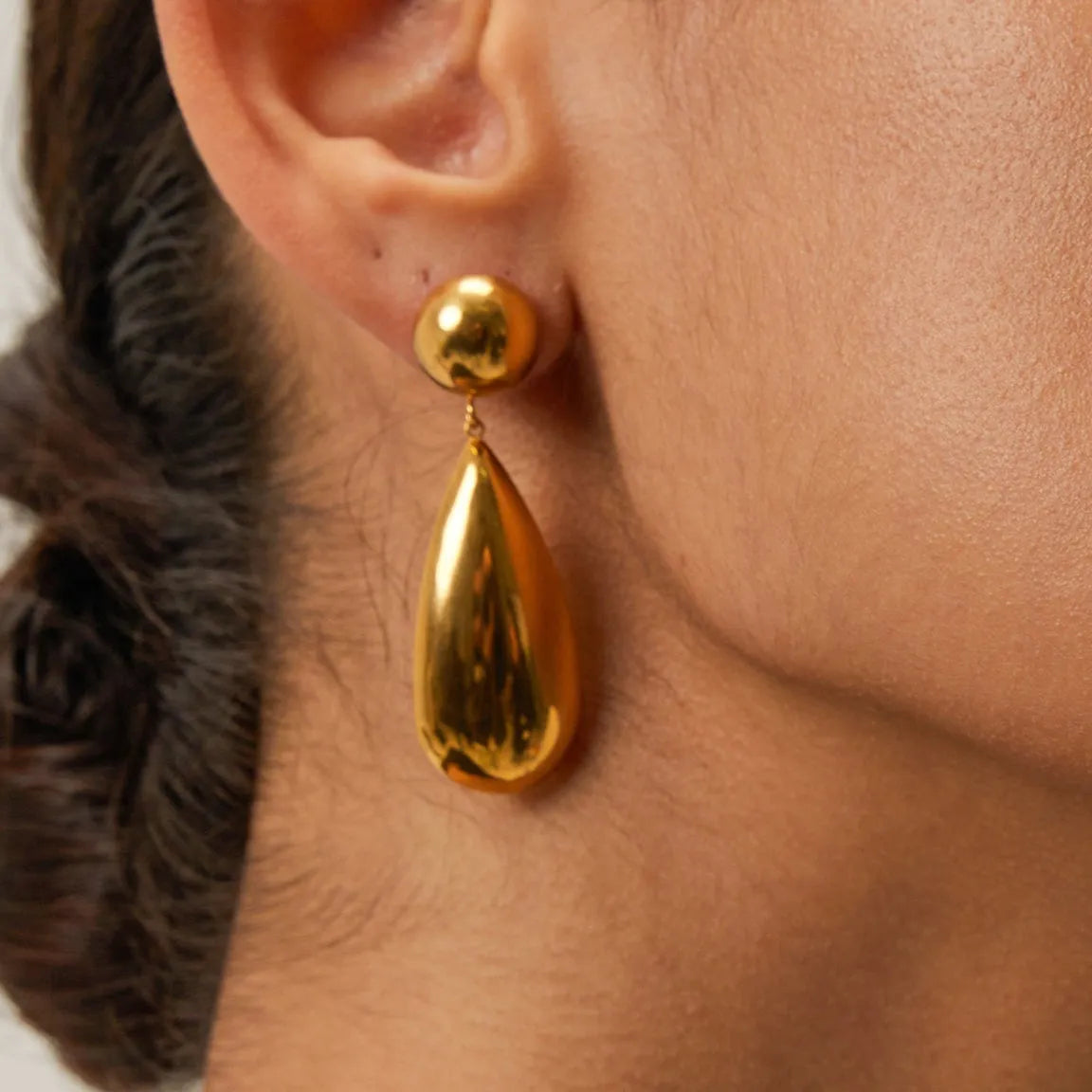 A pair of gold-coloured stainless steel earrings featuring geometric hemisphere shapes forming a water droplet design.
