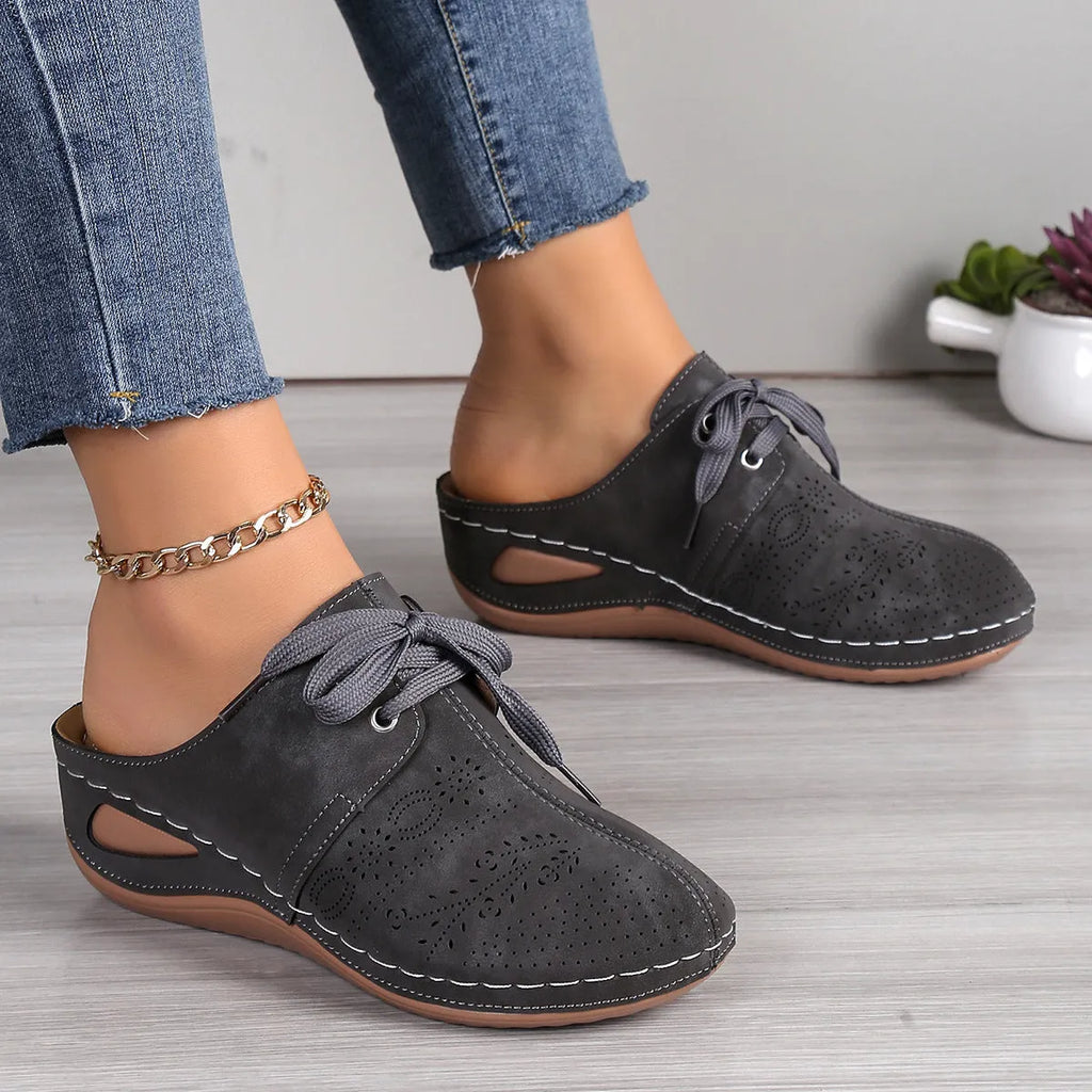 Women's lace-up suede wedge slippers with a hollow-out design, shown in a light colour on a foot.