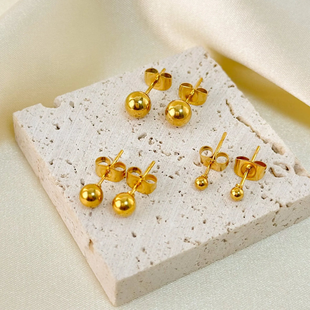 Minimalist round ball stud earrings in gold and silver tones on a plain background.