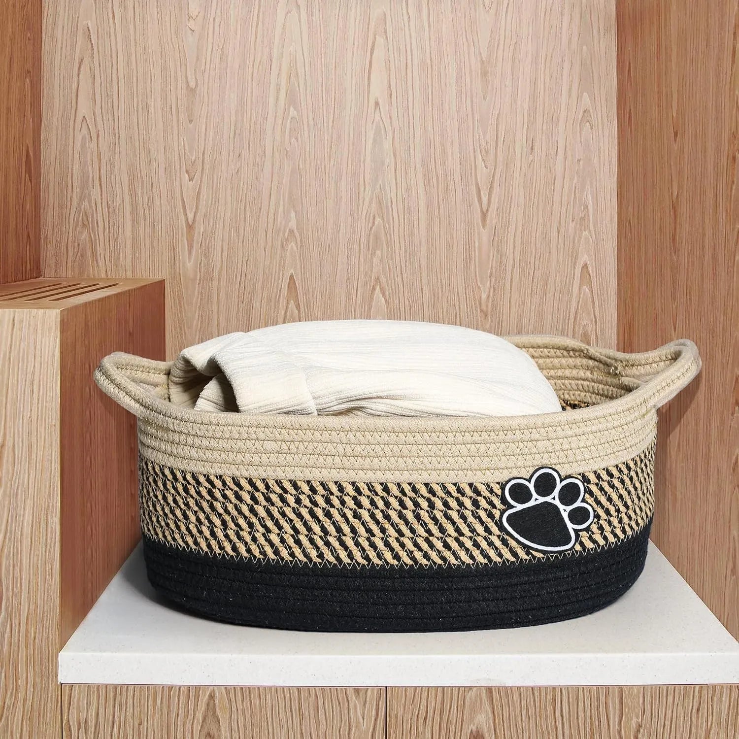 Handmade light beige woven cotton rope storage basket with a handle, shown on a wooden surface.