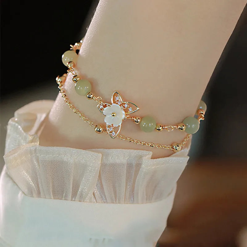Yellow gold electroplated women's bracelet with butterfly and shell flower charms on a chain.