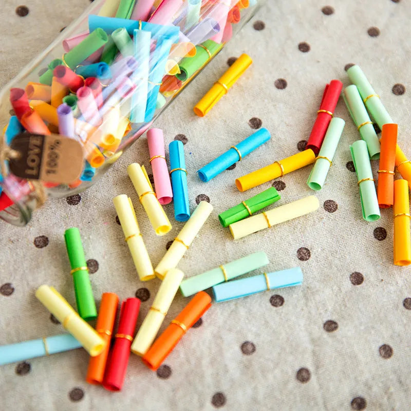Assorted coloured mini paper scrolls for drift bottle messages with metal eyelets, shown in different sizes.