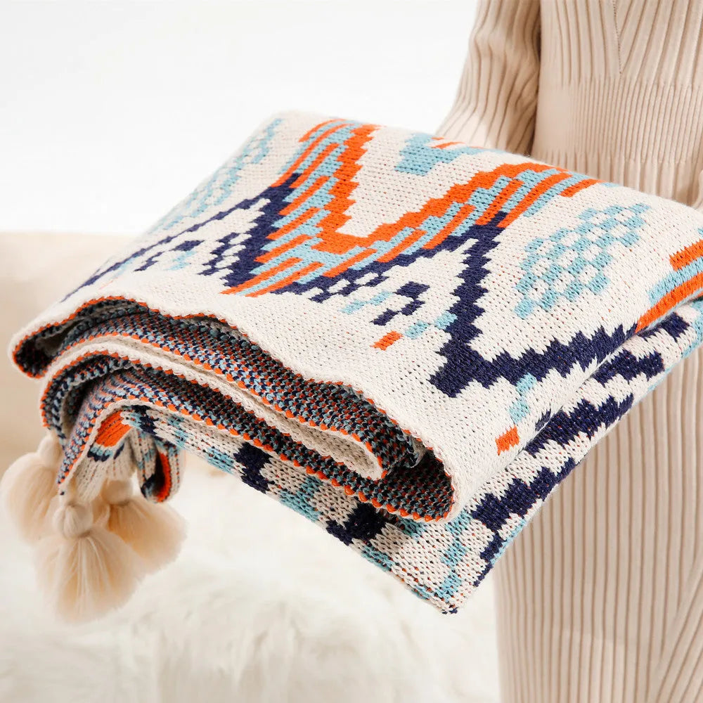 Bohemian-style acrylic sofa blanket with tassel trim shown in a beige and orange colour.