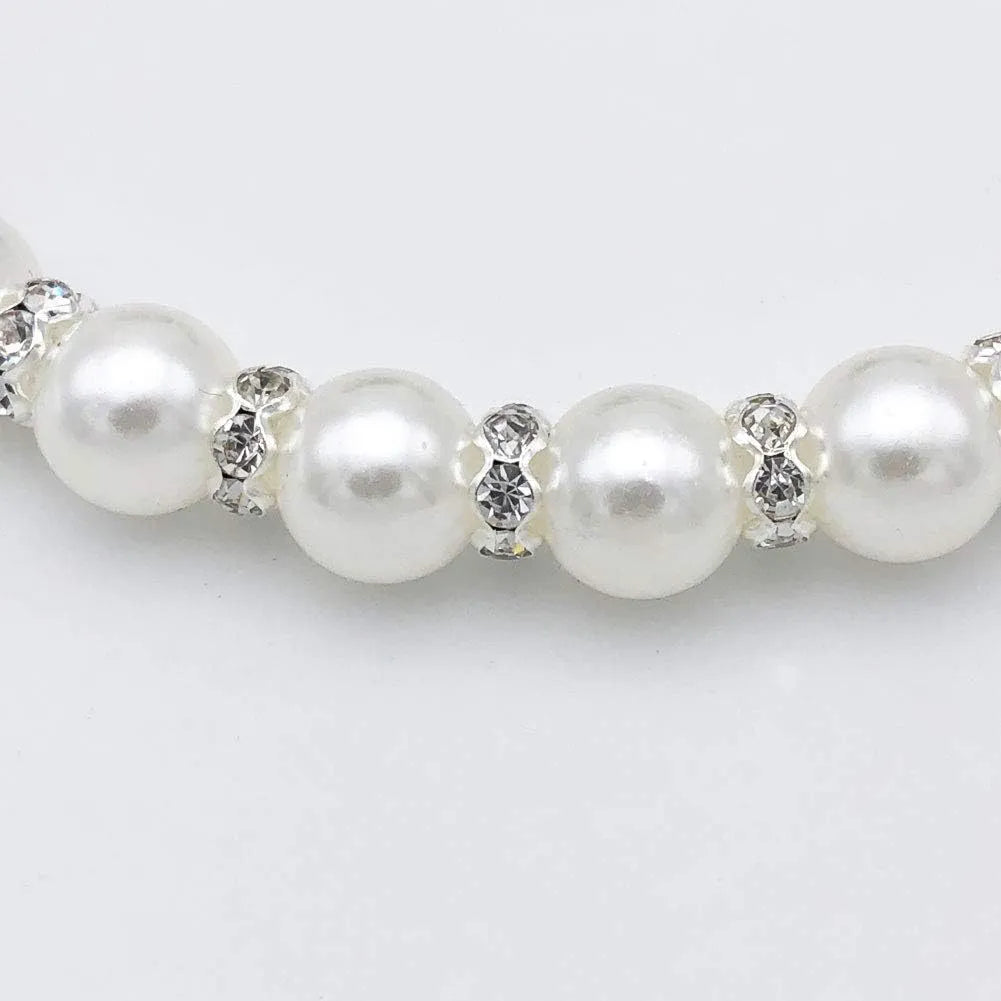 Small dog wearing a blue adjustable pearl and rhinestone necklace collar with a ribbon bow.