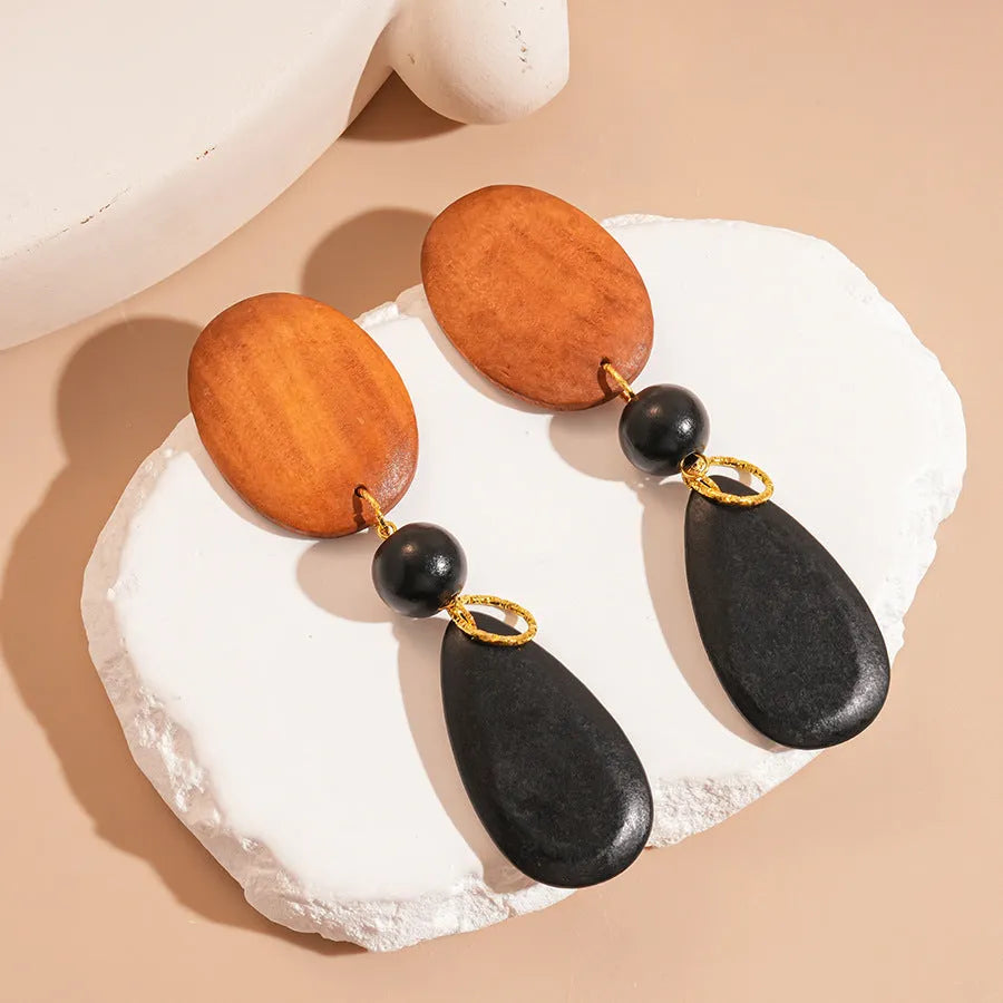 A pair of handmade brown and black wooden elliptical earrings in a retro style.