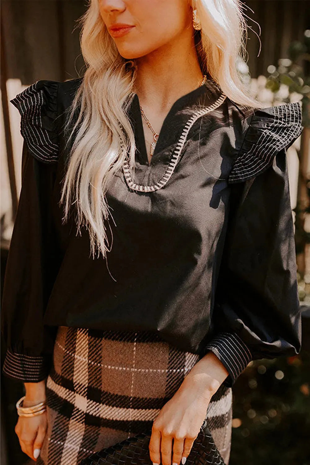 Black women's V-neck blouse with contrast stitching and ruffled long sleeves.