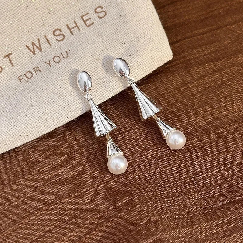 Gold electroplated copper geometric fringe earrings on a woman with long wind chime pearl mosquito coil plate shape close up