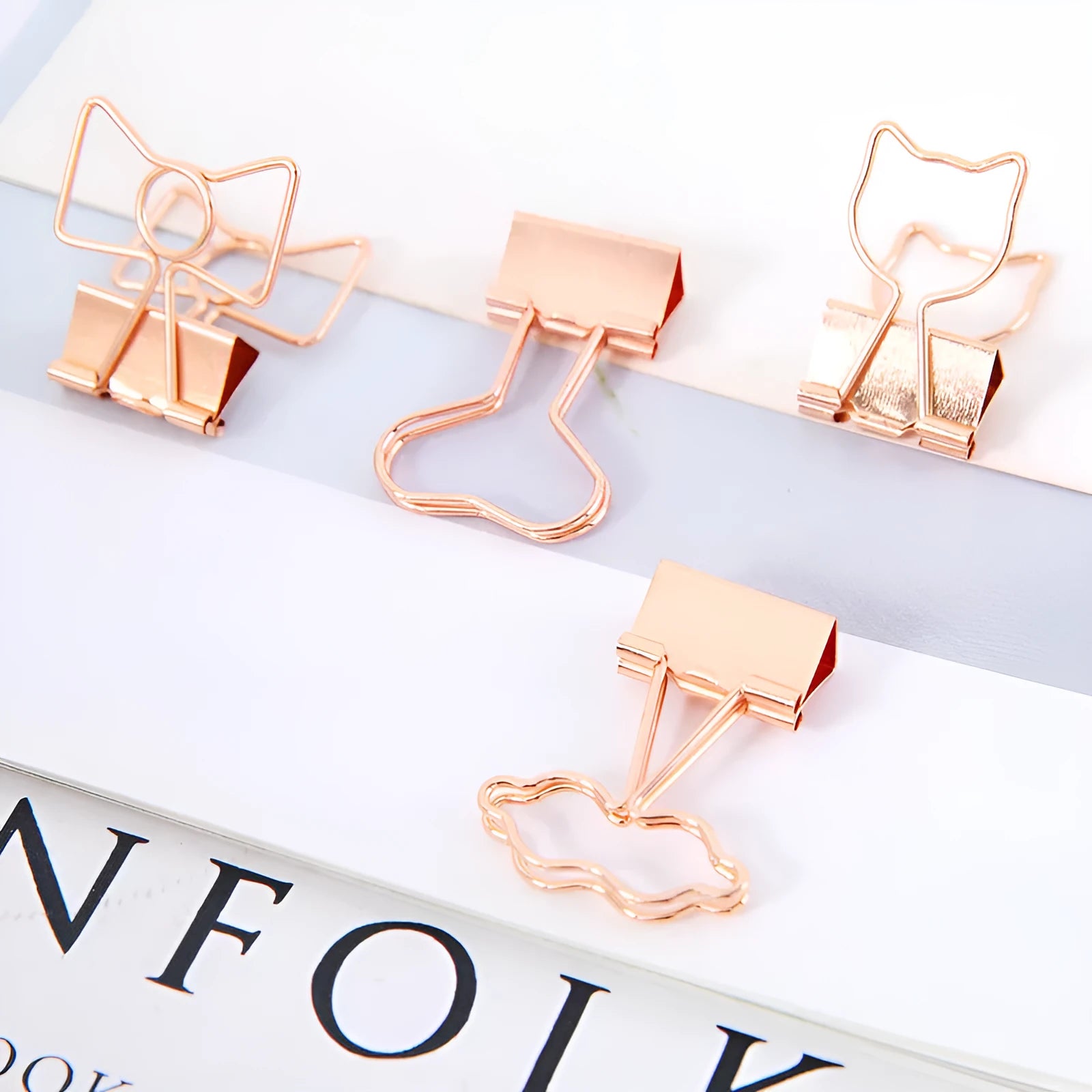 Small gold metal office clip with a long tail handle, shown in decorative bow, cactus, cat, flamingo, and love shapes.