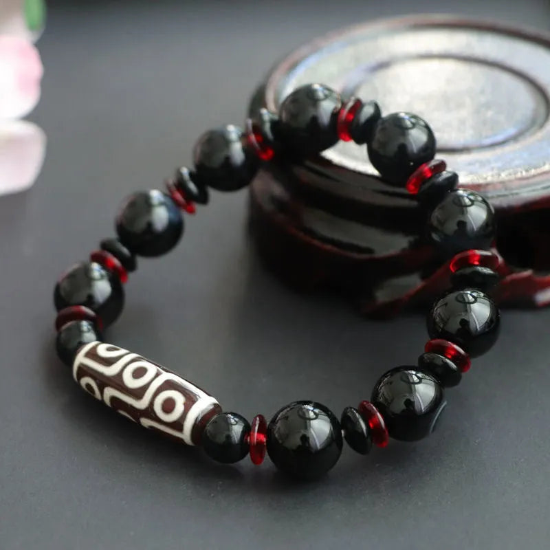 Close-up of a hand-woven black agate dzi bead bracelet with 11mm geometric beads on a wrist.