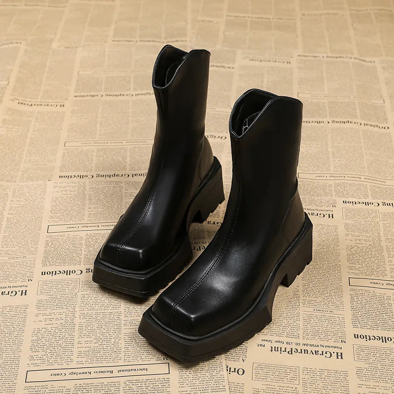 Black platform Martin ankle boots with a square toe, chunky heel, and back zipper on a woman's feet.