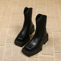 Black platform Martin ankle boots with a square toe, chunky heel, and back zipper on a woman's feet.
