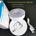 Small circular white motion sensing LED night light with USB charging cable and adhesive tape.