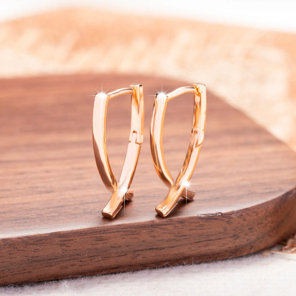 Rose gold coloured cross-shaped drop earrings for women on a white background.