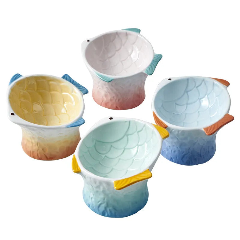 Blue fish-shaped ceramic cat bowl with tilted angle and elevated base on a table.