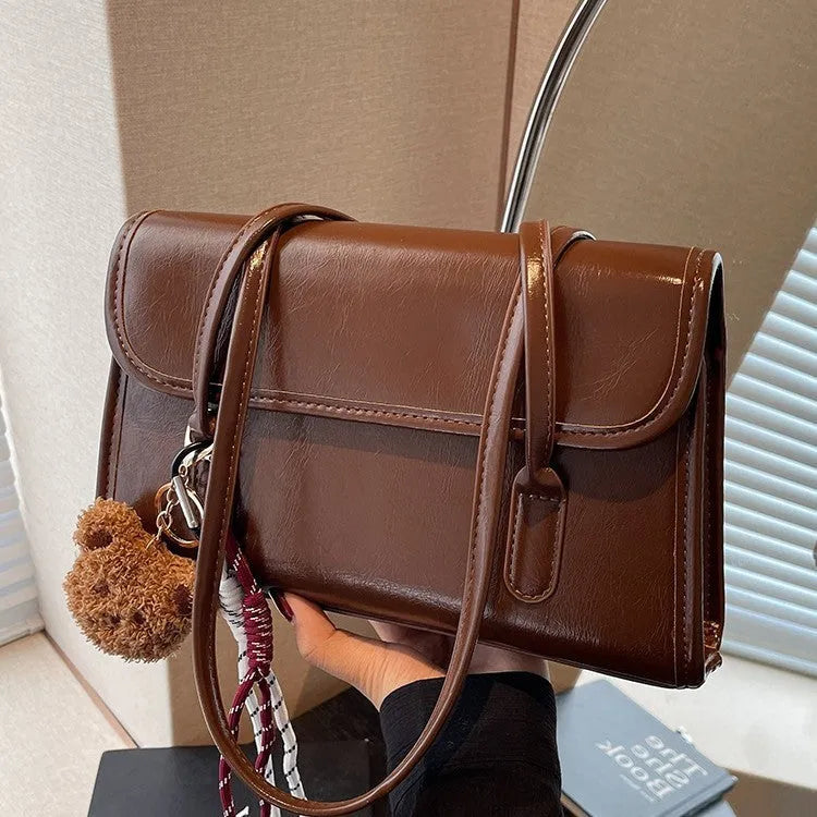 Brown women's square shoulder bag with pendant detail and adjustable crossbody straps on table