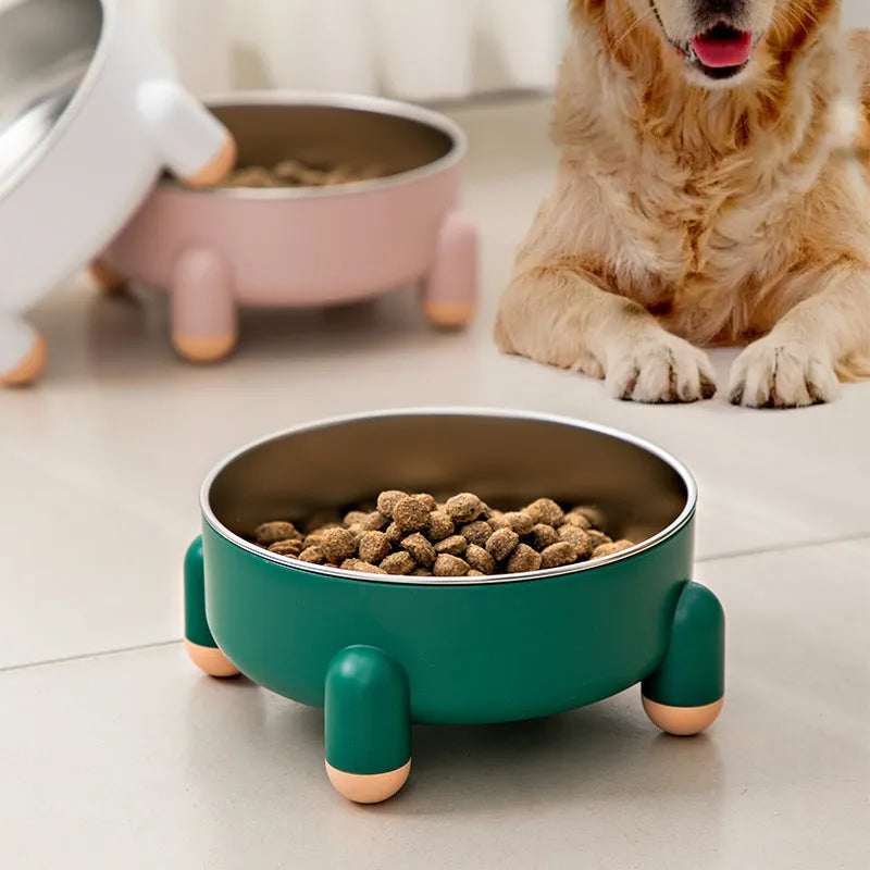 Green stainless steel pet bowl with a non-slip rubber ring and raised foot design on a wooden floor.