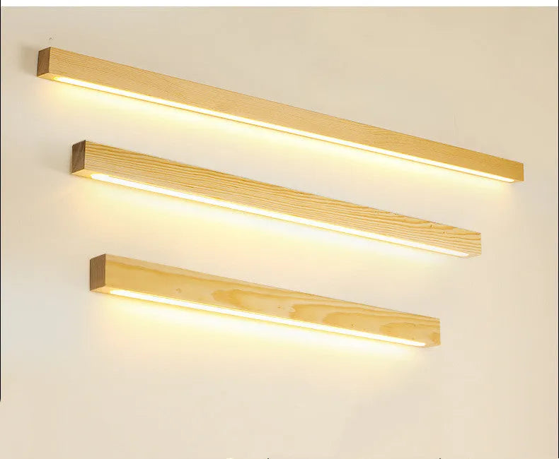 Walnut colour wood and acrylic strip wall lamp in three lengths on a white wall.