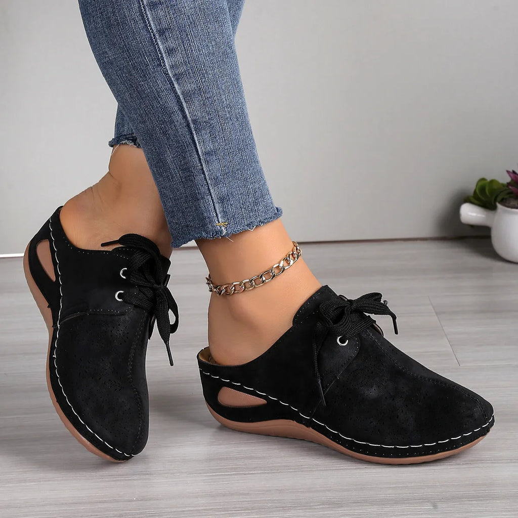 Women's lace-up suede wedge slippers with a hollow-out design, shown in a light colour on a foot.