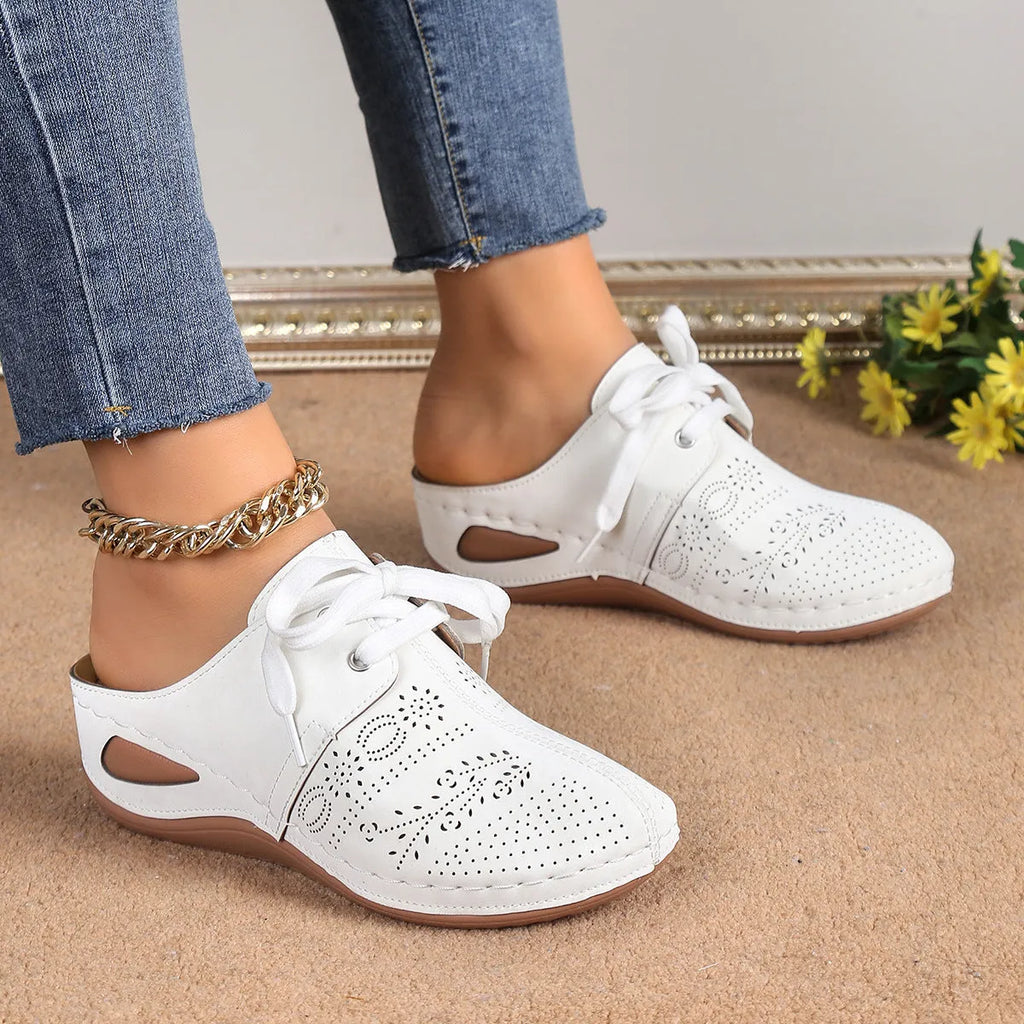 Women's lace-up suede wedge slippers with a hollow-out design, shown in a light colour on a foot.