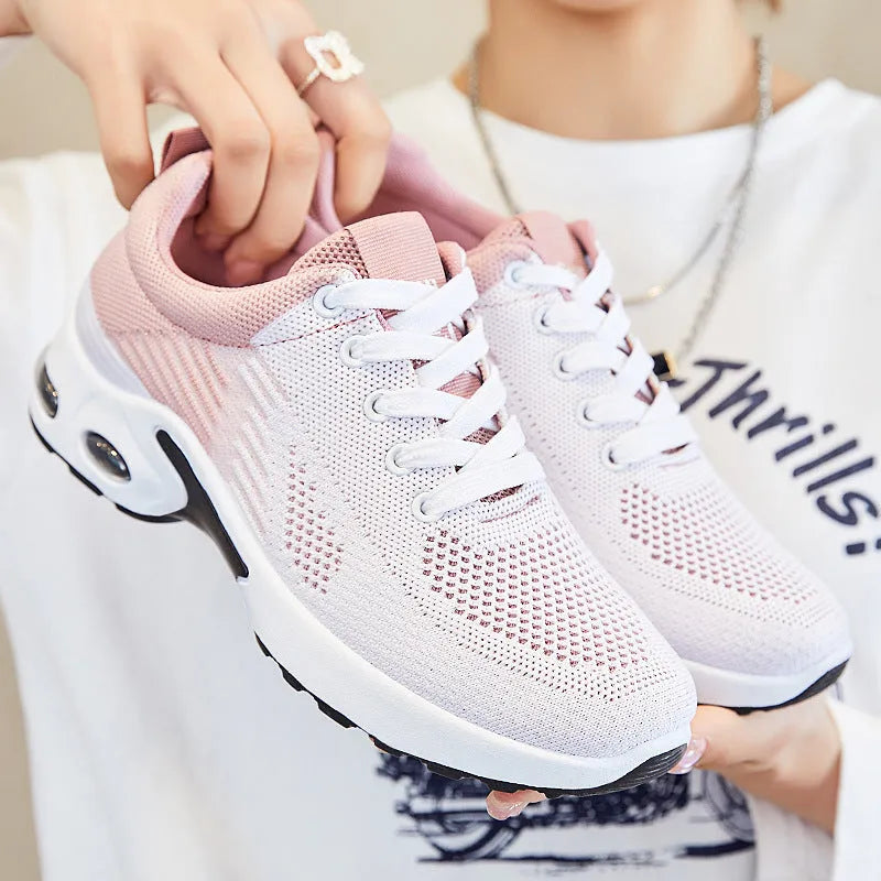 Women's pink flyknit running shoes with lace-up front, mesh lining, and flat PVC sole on a striped background.