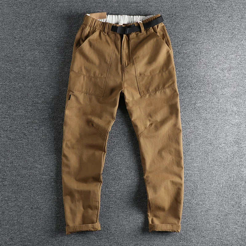 Man wearing mid-waist khaki cotton work trousers with a zipper fly and straight leg cut.