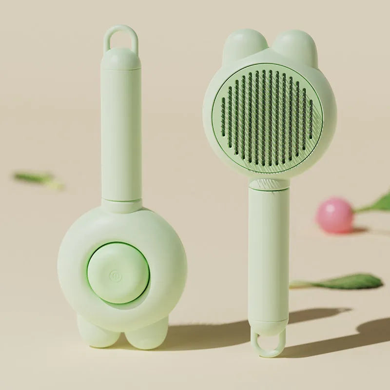 Green self-cleaning cat brush with metal comb and release button for pet grooming.