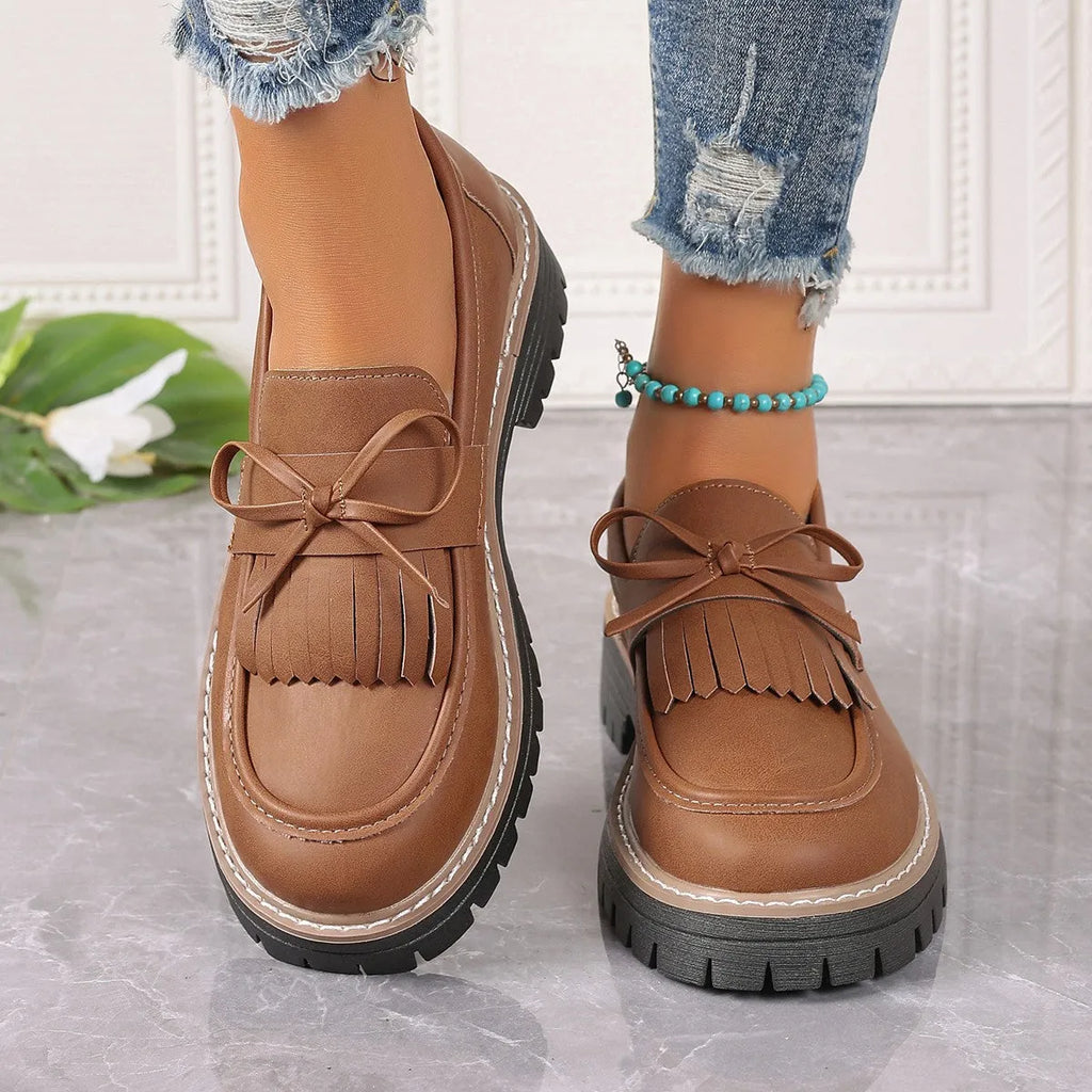 Black and brown women's loafers with a tassel bow detail and a chunky low heel.