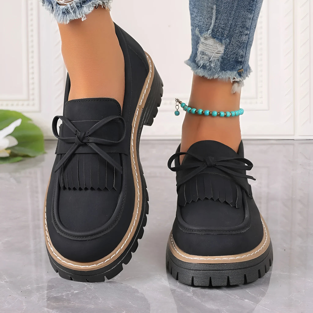 Black and brown women's loafers with a tassel bow detail and a chunky low heel.