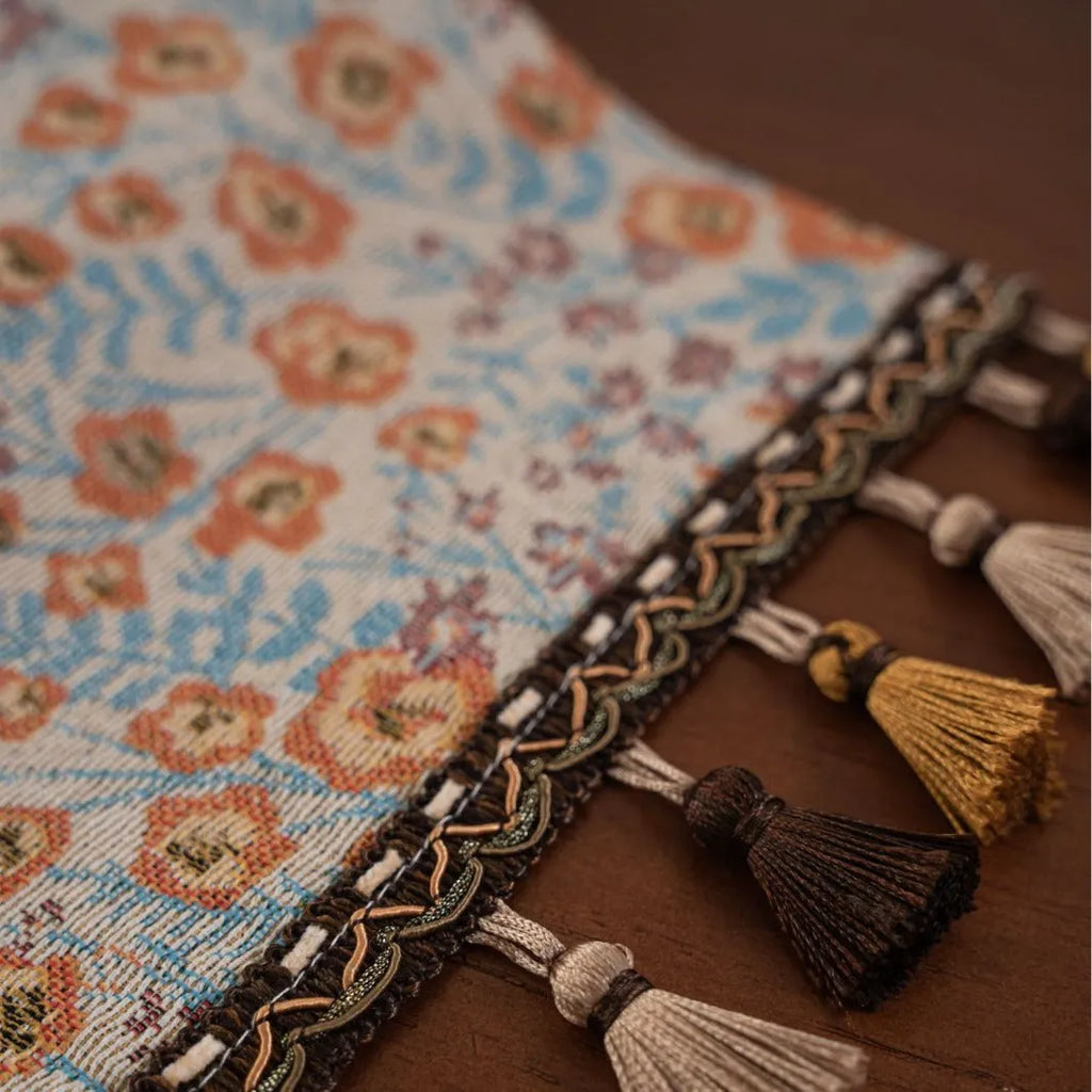 Beige jacquard table runner with long tassels and floral leaf pattern laid on a dining table.