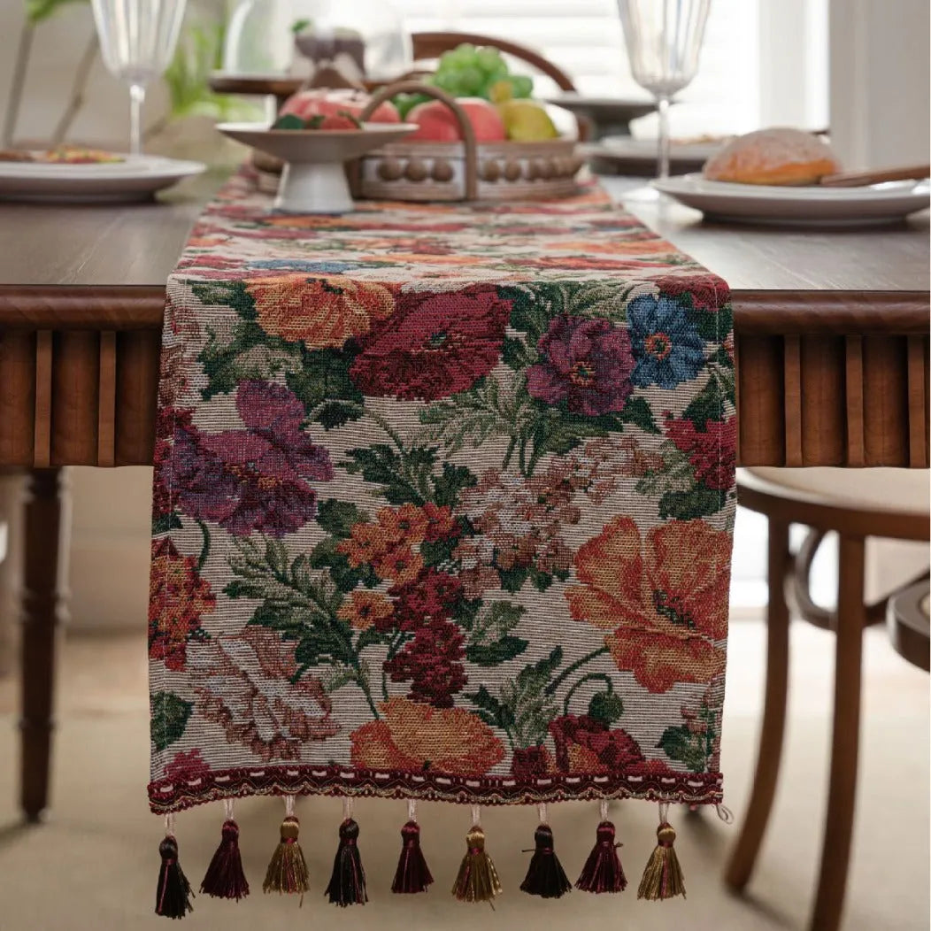 Beige jacquard table runner with long tassels and floral leaf pattern laid on a dining table.
