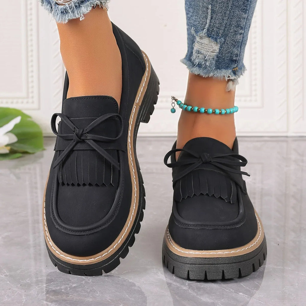 Black and brown women's loafers with a tassel bow detail and a chunky low heel.