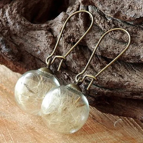 Close-up of transparent glass dandelion seed earrings on a French hook in silver finish.