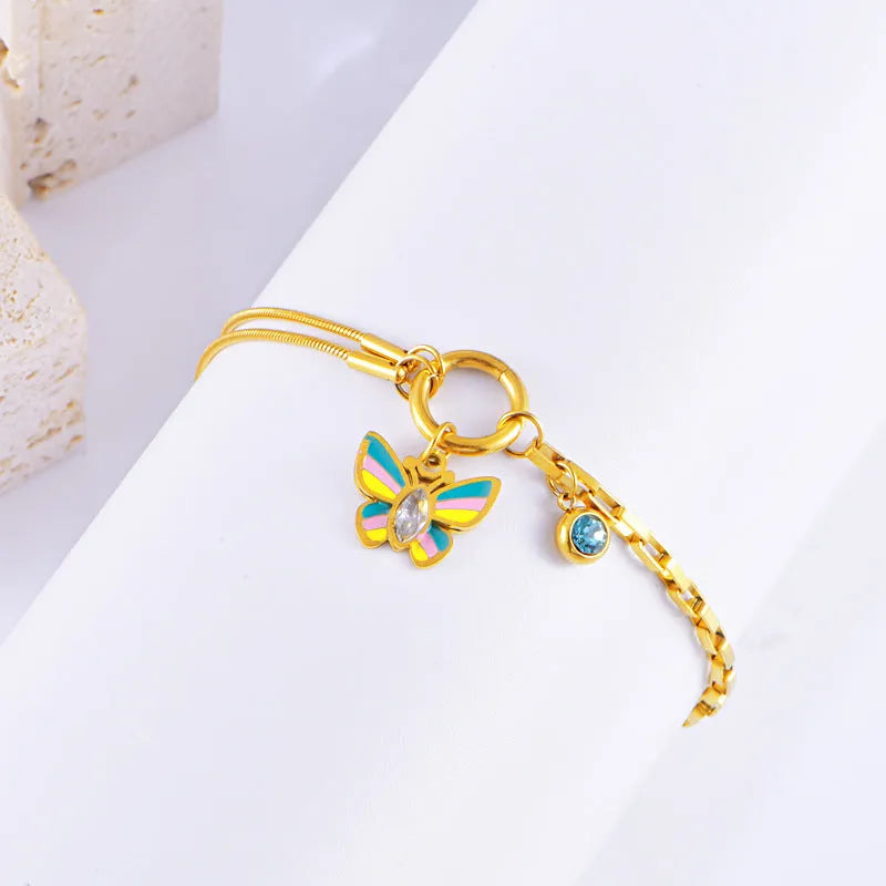 Gold titanium steel butterfly necklace and matching bracelet set on a dark background.
