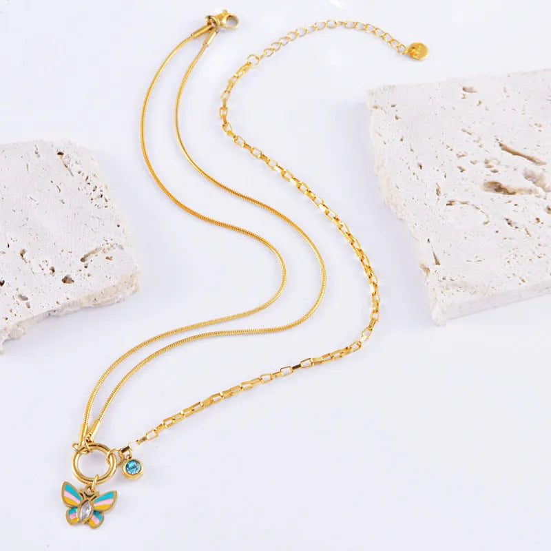 Gold titanium steel butterfly necklace and matching bracelet set on a dark background.