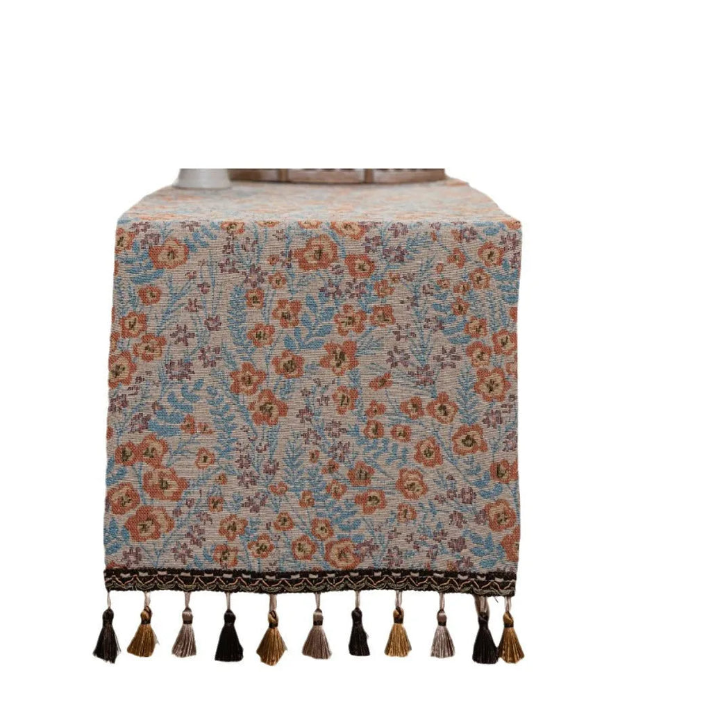 Beige jacquard table runner with long tassels and floral leaf pattern laid on a dining table.