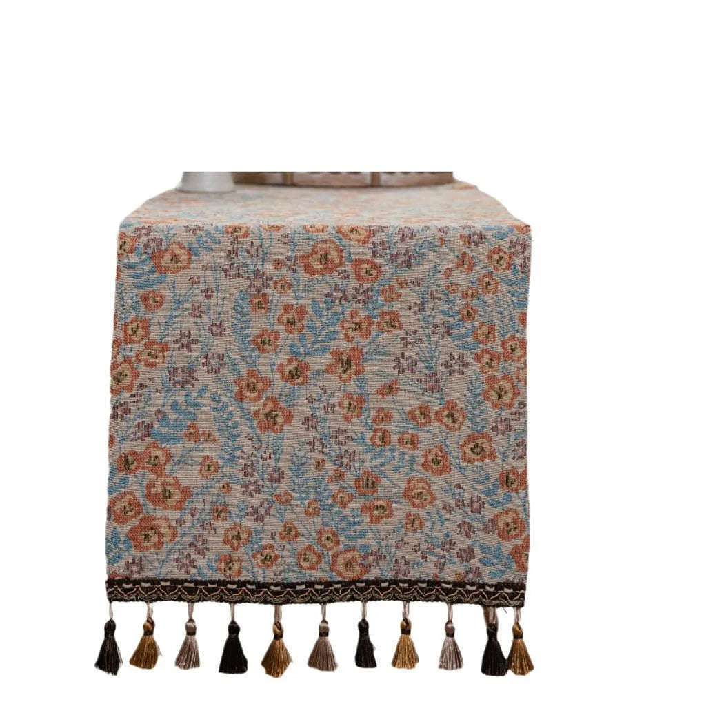 Beige jacquard table runner with long tassels and floral leaf pattern laid on a dining table.