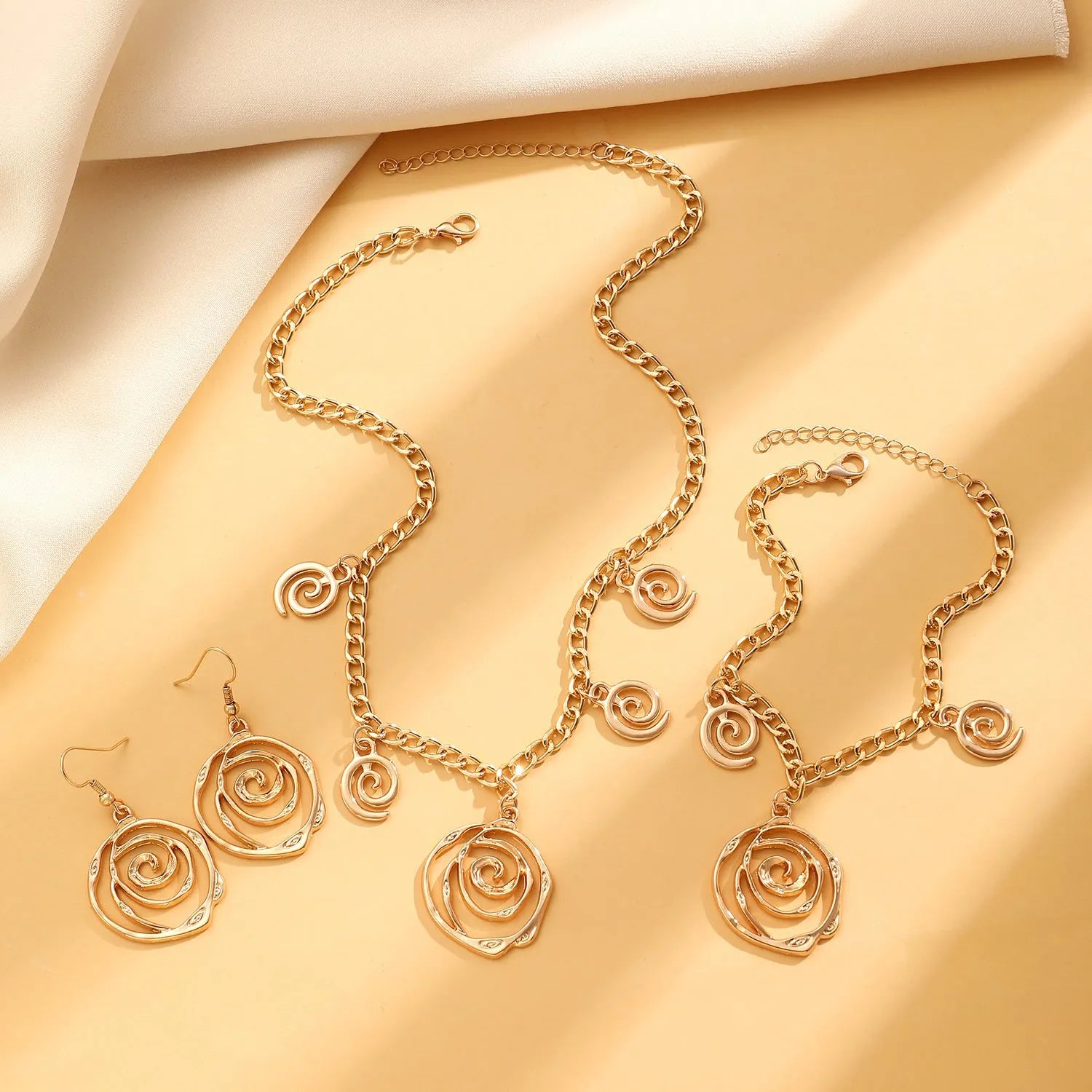 Gold spiral donut geometric jewellery set with adjustable necklace, matching bracelet, and earrings on a white background.