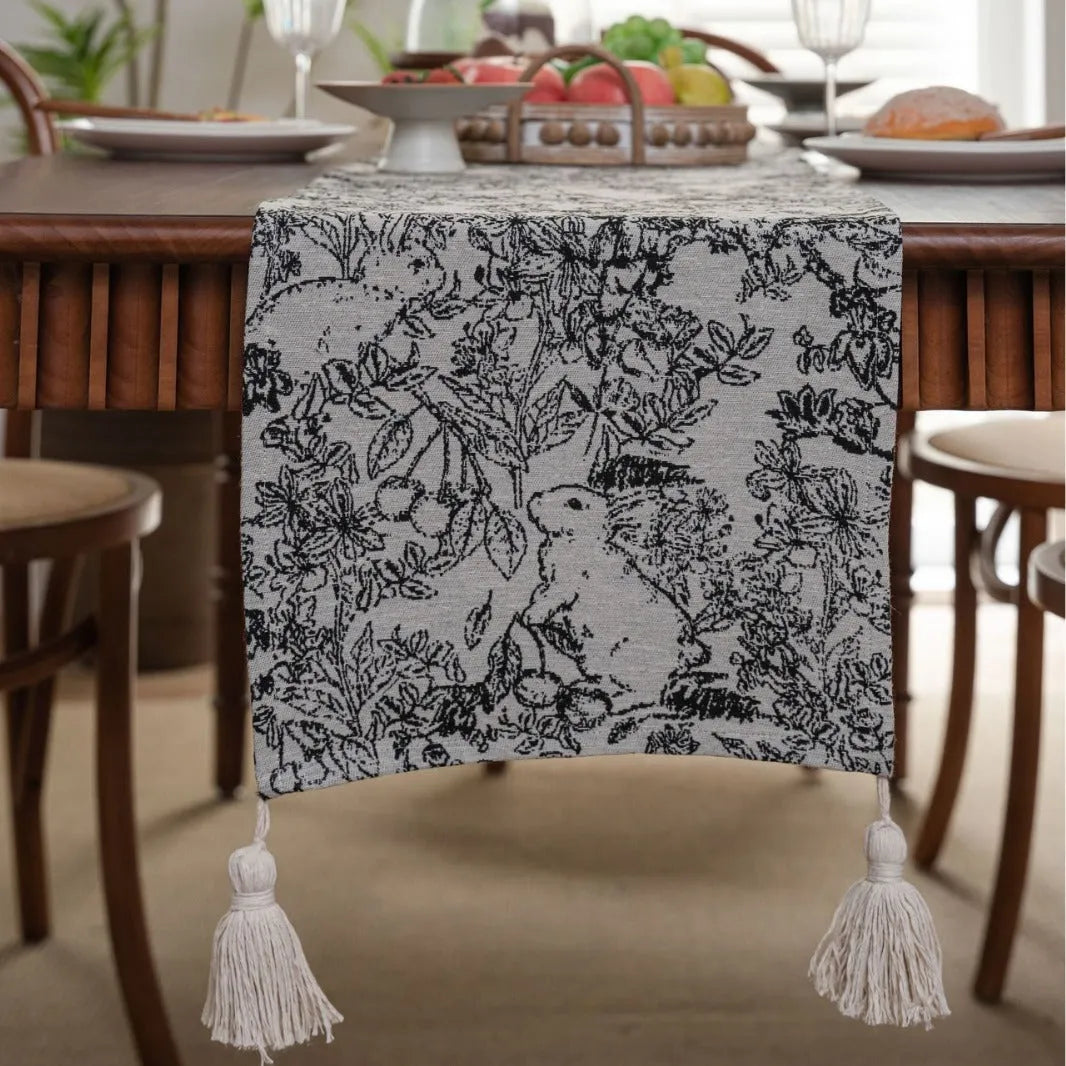 Beige jacquard table runner with long tassels and floral leaf pattern laid on a dining table.