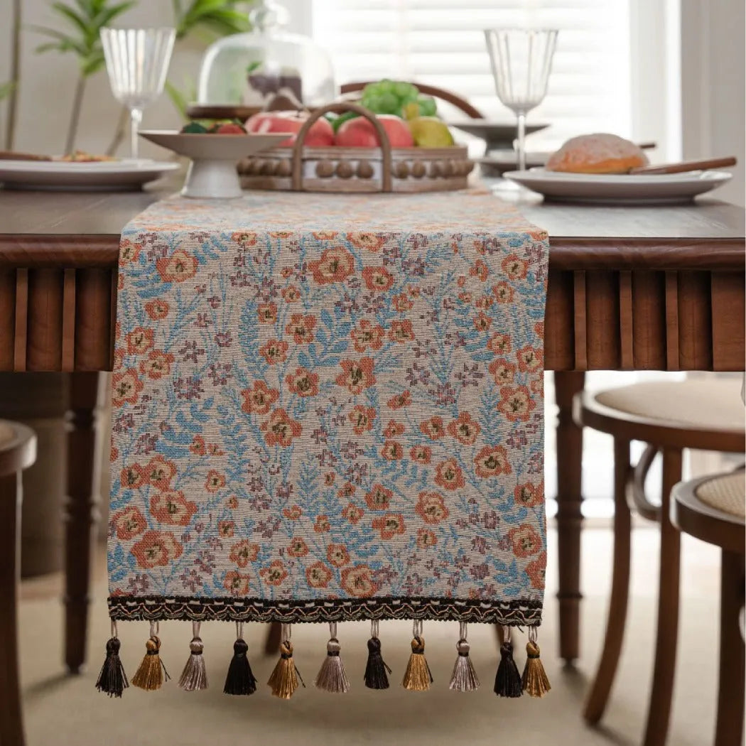 Beige jacquard table runner with long tassels and floral leaf pattern laid on a dining table.