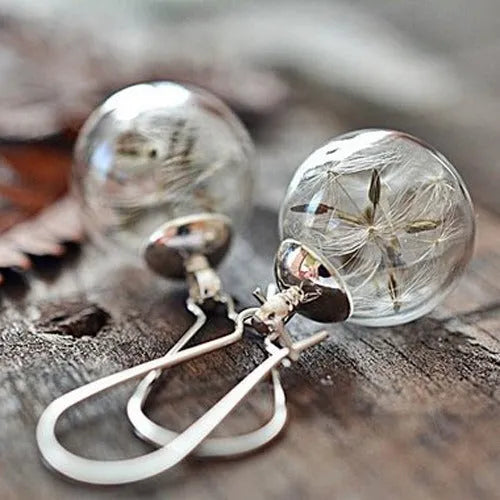 Close-up of transparent glass dandelion seed earrings on a French hook in silver finish.