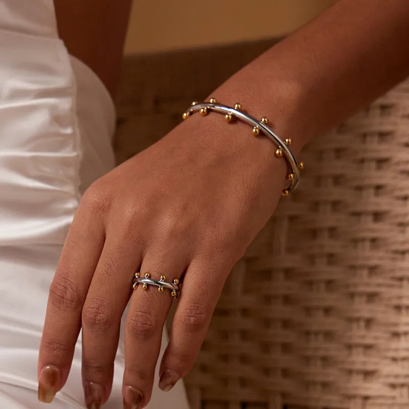Stainless steel C-shaped bracelet with textured rivet bean beads in gold or steel colour.