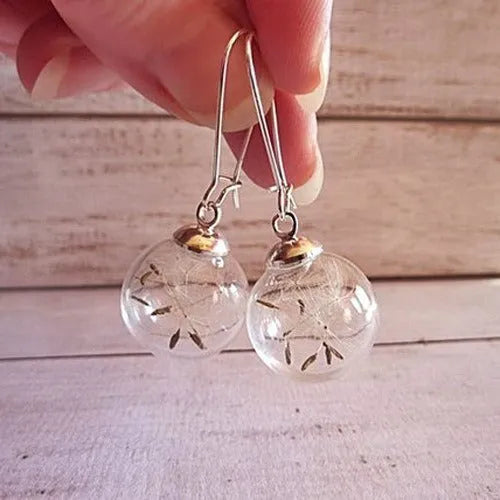 Close-up of transparent glass dandelion seed earrings on a French hook in silver finish.