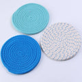 Three round blue cotton cord coaster placemats on a wooden table.