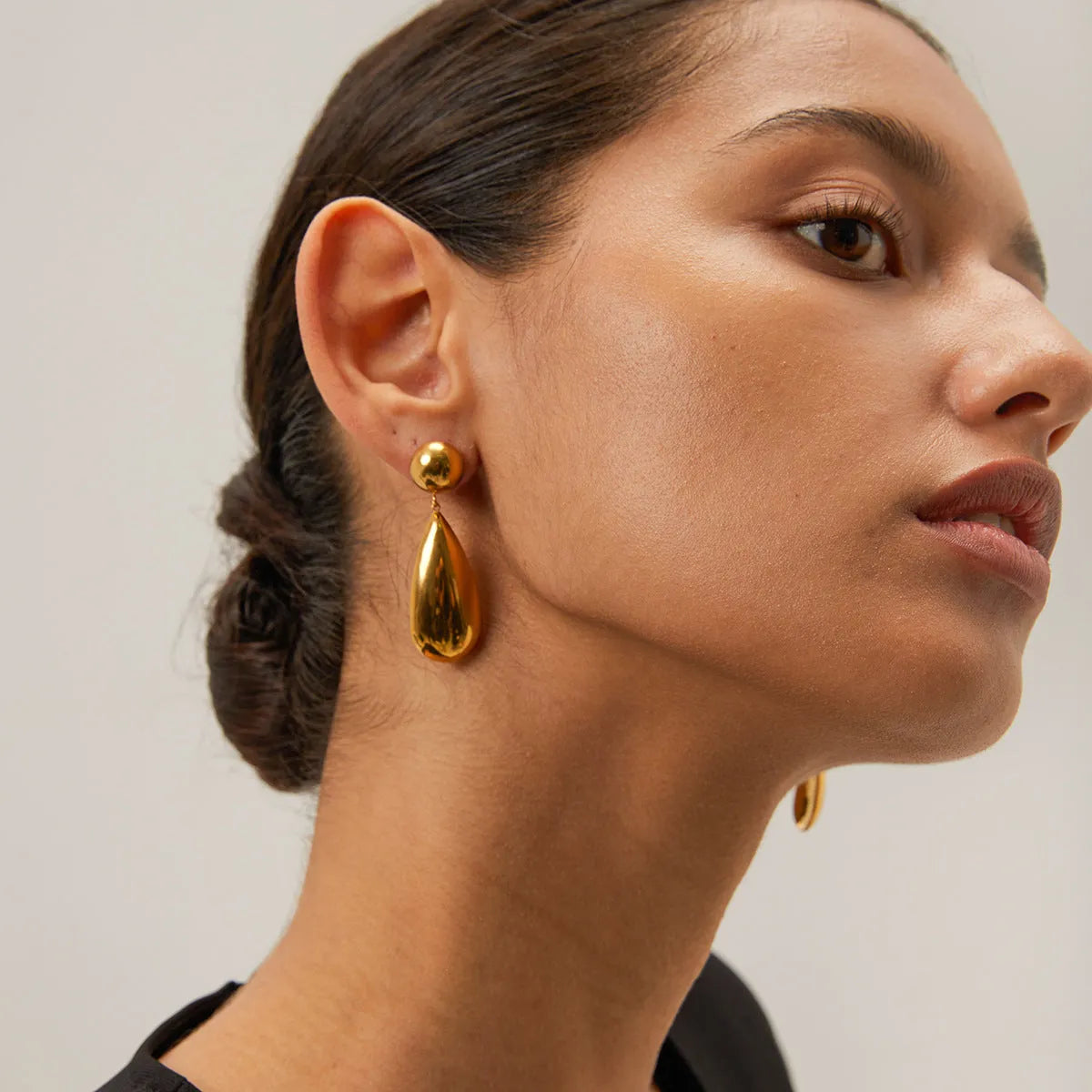 A pair of gold-coloured stainless steel earrings featuring geometric hemisphere shapes forming a water droplet design.