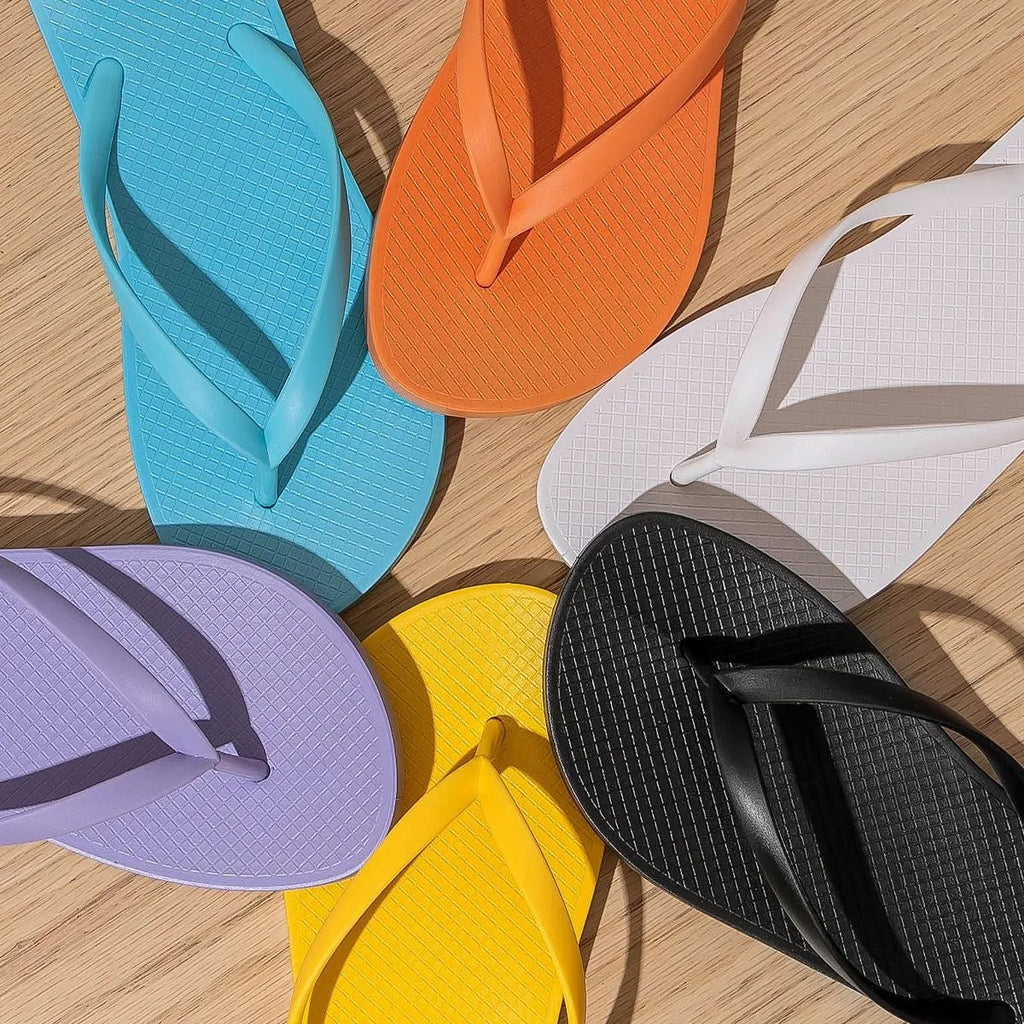 Orange foldable plastic beach slippers with a non-slip hollow-out PVC sole on a sandy background.